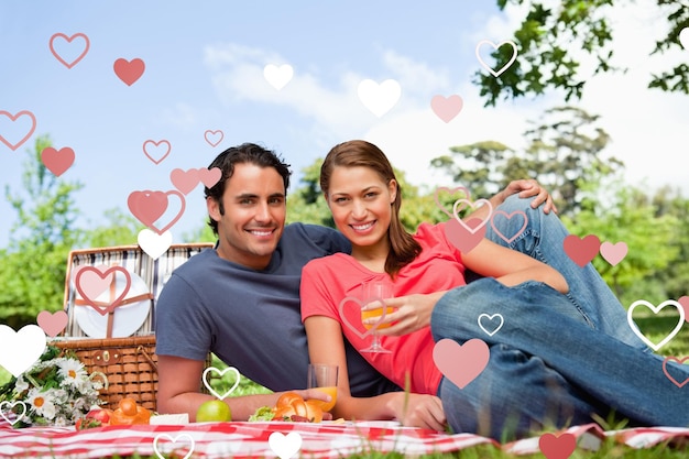 Two friends looking ahead while they hold glasses as they lie on a blanket against valentines heart design