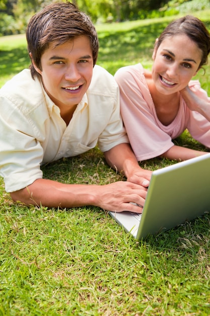 Two friends looking towards the side while using a laptop