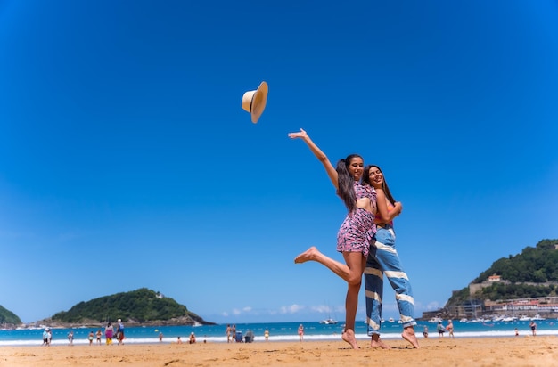 喜びの海のライフスタイルの帽子を投げてビーチで夏休みに2人の友人