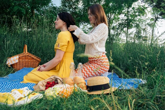 Two friends at picnic one braids the other's hair