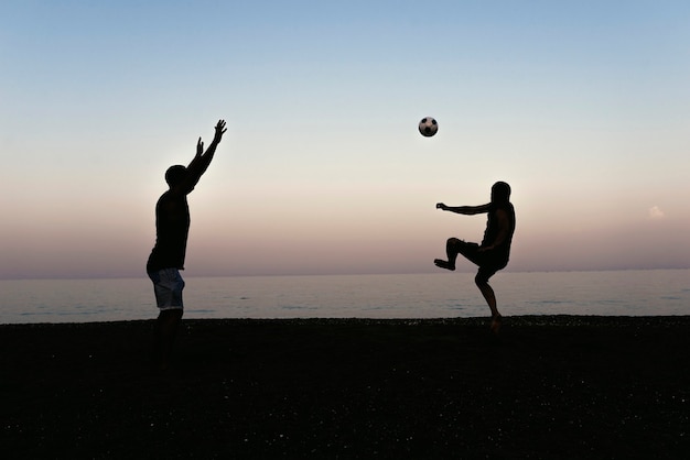 Two friends playing soccer in the beach.