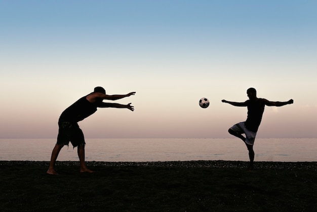 Photo two friends playing soccer in the beach.