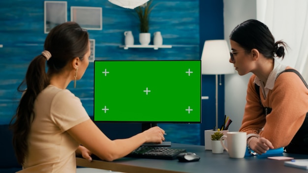 Due amici seduti davanti al computer mock up chroma key schermo verde. donna d'affari che lavora alla pubblicità commerciale utilizzando il pc isolato dell'ufficio domestico