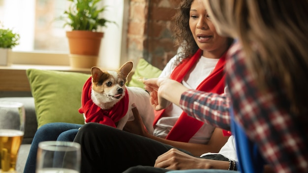 Two friends sitting on the sofa feeding a dog.