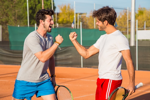 Two friends standing on tennis court and encouraging each other before match. 