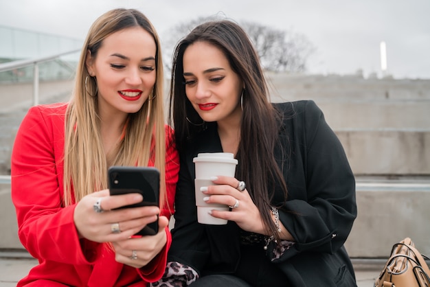 Due amici che utilizzano il loro telefono cellulare seduti all'aperto