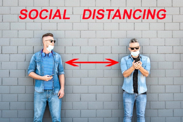 Two friends wearing lowered face protective masks using smart mobile phones while keeping social distance to prevent COVID19 coronavirus disease Social distancing concept new normal Banner