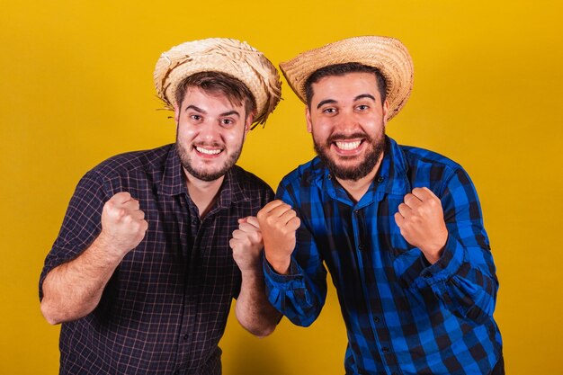 Двое друзей в типичной одежде для праздника Festa Junina в Аррайя-де-Сан-Жуан аплодируют, празднуя победу