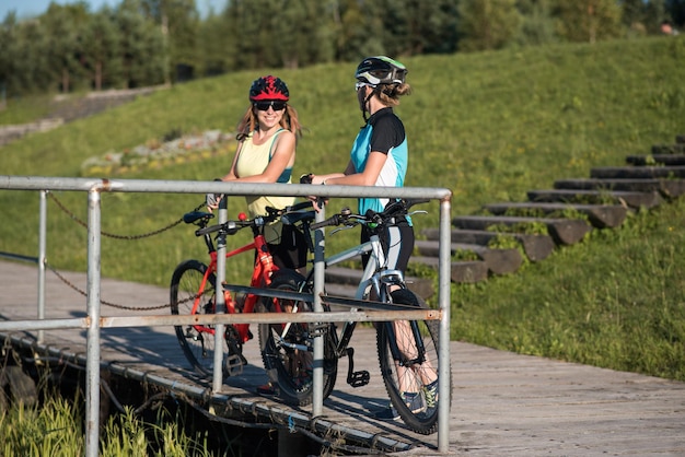 Two friens female with bikes standing on the pierce and looking at the water