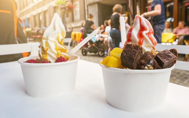 two frozen yoghurt cups with brownie and fruits toppings on a restaurant table