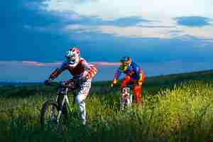 Photo two fully equipped professional downhill cyclists riding bikes on the summer trail