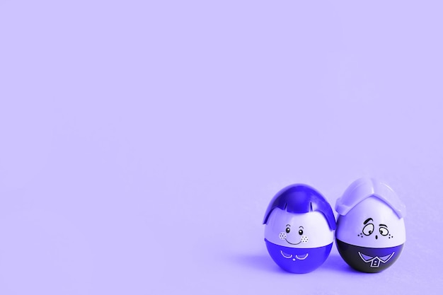 Two funny eggs boy and girl with faces on a purple background - Easter, spring. Tinting very peri. Children's toys-a symbol of a couple of men and women, love, family. Copy space.