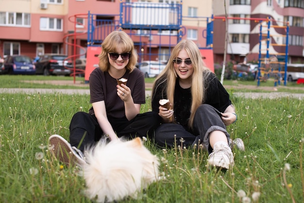 Photo two funny girls are eating ice cream and playing with a pomeranian dog holidays