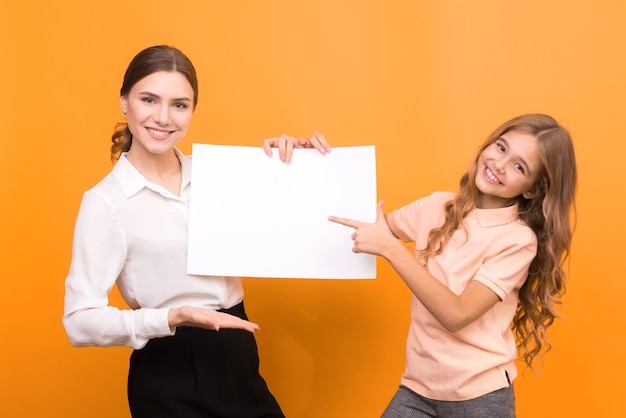 Photo two funny girls holding clear sheet of paper on orange background mock up