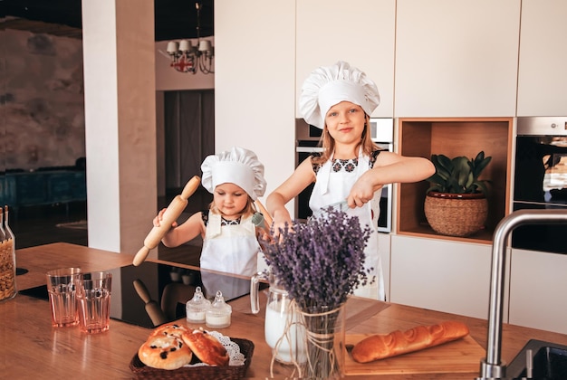 Two funny girls in the kitchen wearing a chef's hat and white apron playing in the kitchen