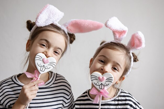 Two funny little sisters are posing with Easter gingerbread in the form of bunny faces.