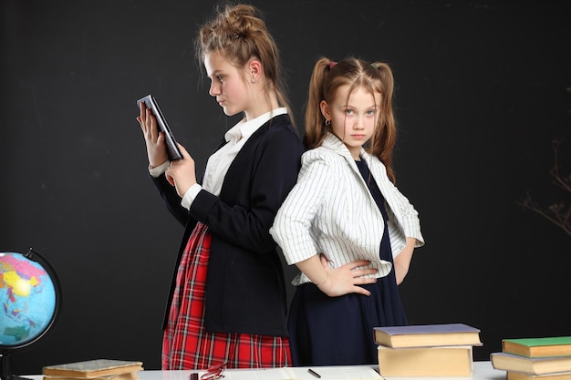 制服を着た2人の面白い女子学生が本のある黒板の背景に座っています