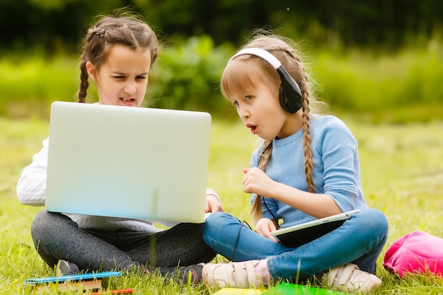 two funny schoolgirls sit on the grass and read books. Girls, girlfriends, sisters are taught lessons in nature.