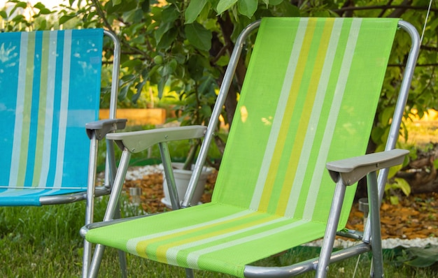 Due sedie pieghevoli da giardino stanno all'ombra sotto un albero in una calda giornata estiva nel primo piano del giardino