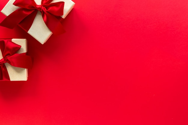 Two gift boxes with a red bow on a red, top view with copy space