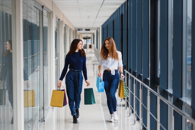 Two girl-friends on shopping walk on shopping centre with bags