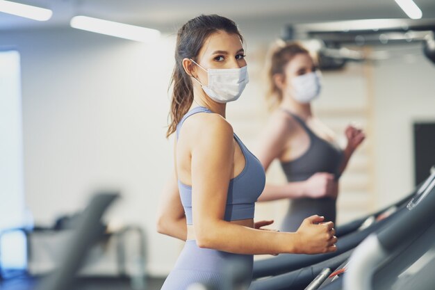 two girl friends working out on treadmill in masks due to covid-19