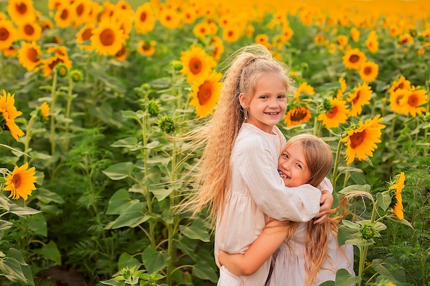 two girlfriends girls longhaired blondes in linen dresses hugging on a sunflower field