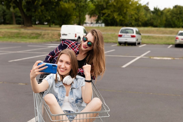 Two girlfriends having fun in a supermarket parking lot.