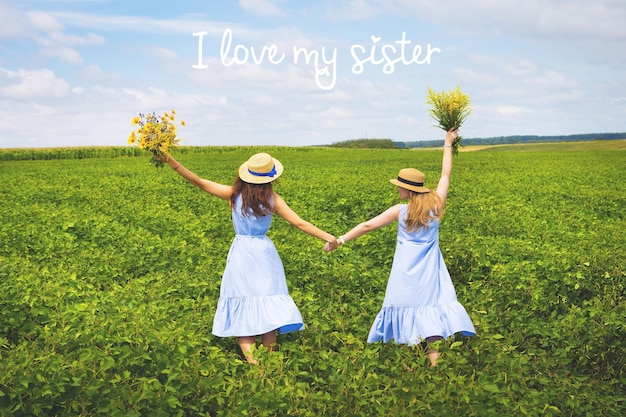 Two girlfriends holding hands with a bouquet of yellow flowers in a green fieldinscription I love my sister