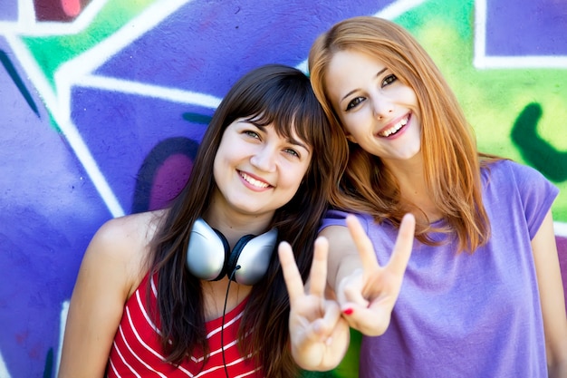 Two girlfriends near graffiti wall.