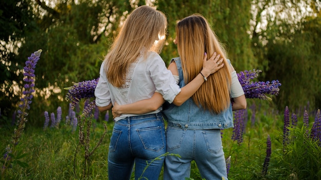 Two girlfriends standing on the field with bouquets of purple flowers