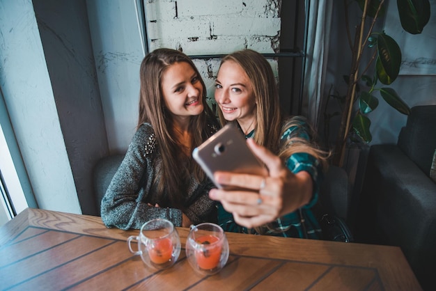 Two girlfriends taking selfie while sitting in cafe