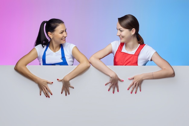 Две девушки в фартуках позируют с белым рекламным щитом. рекламная концепция