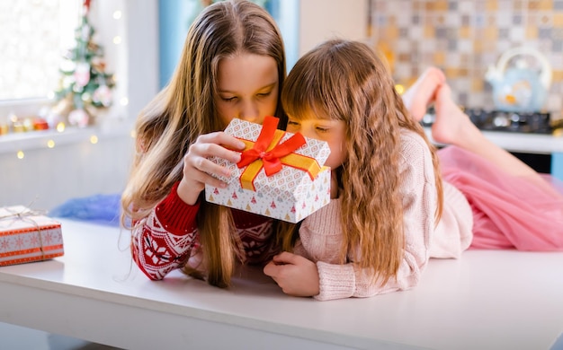二人の女の子が台所に座って、贈り物と一緒に箱を振っています