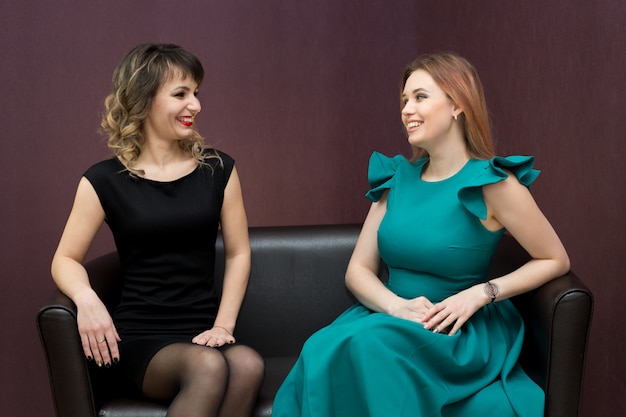 Two girls are talking while sitting on the couch.