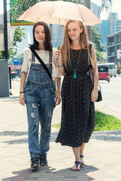 Due ragazze stanno camminando in una giornata calda sotto un ombrello