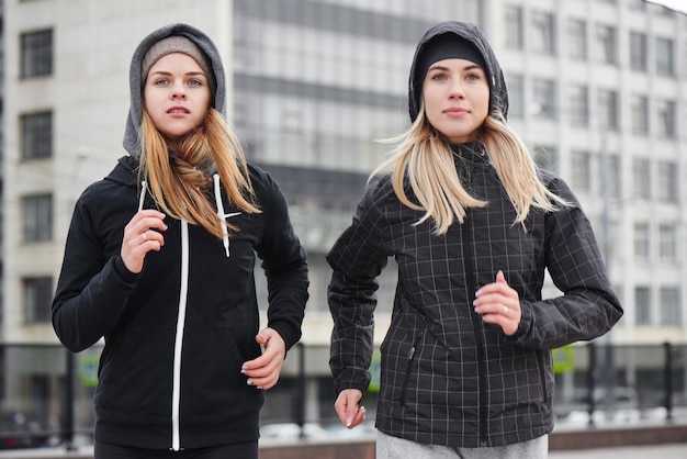 Two girls athletes running down the street in the city. Girlfriends in sports