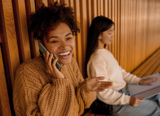 Due ragazze su una panchina, una che studia, un'altra che parla al telefono