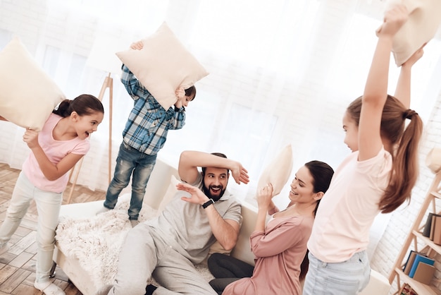 Two girls and a boy fight with pillows with their parents.