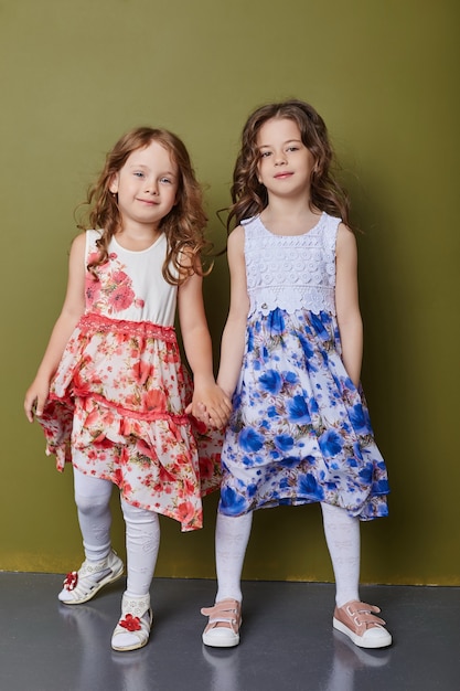 Two girls in bright spring clothes on an olive colored background