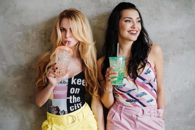 Two girls, a brunette and a blonde, in colorful trousers. drink cocktails.