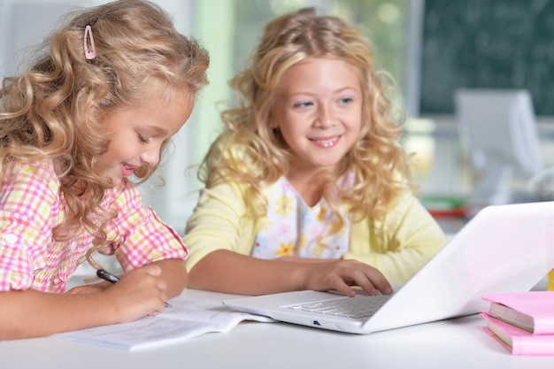 Two girls at class using laptop and writing