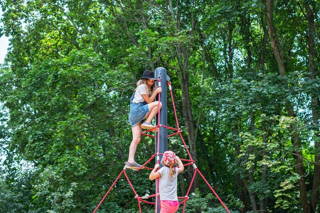 2人の女の子が木々の間の公園でロープピラミッドを登る