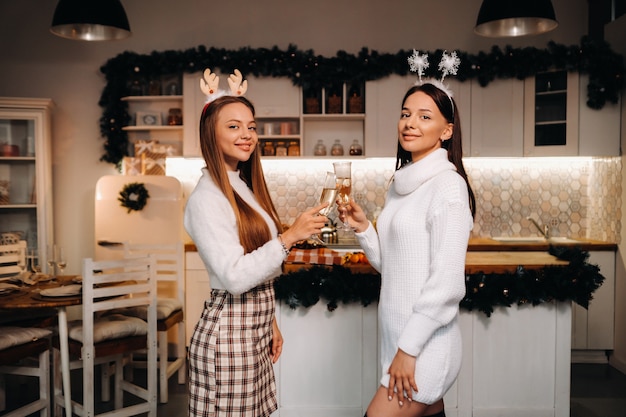 Two girls in a cozy home environment with champagne in their hands at Christmas. Smiling girls drink champagne on a festive evening