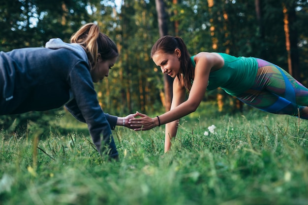 Two girls doing buddy workout outdoors performing push-ups to clap on grass