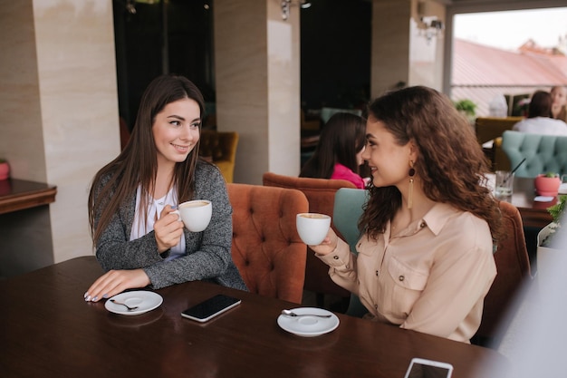 Две девушки пьют кофе в кафе и разговаривают