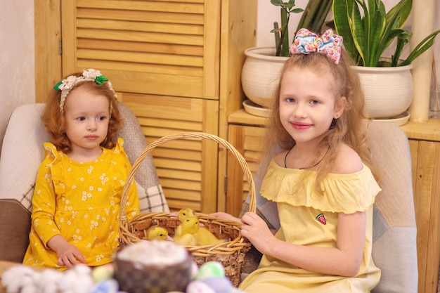 Two girls at Easter with little yellow ducklings Next to the cake and painted eggs Holiday Family Happiness