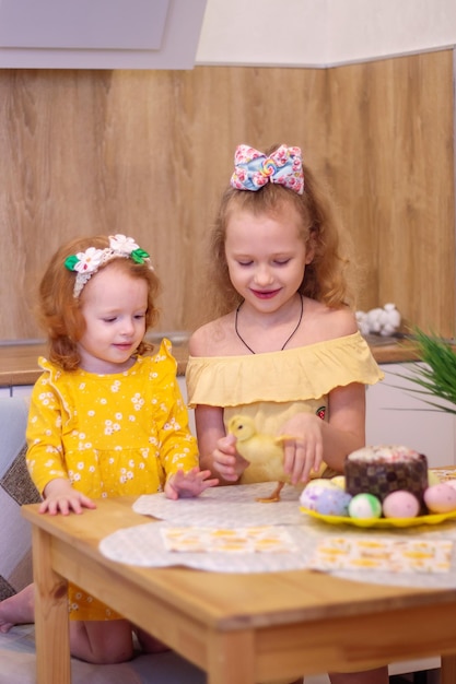 Two girls at Easter with little yellow ducklings Next to the cake and painted eggs Holiday Family Happiness