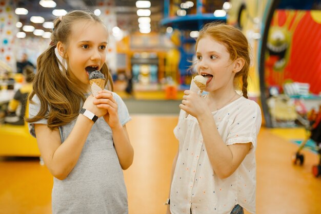 2人の女の子がエンターテインメントセンターでアイスクリームを食べます。休日の子供たちのレジャー、子供の頃の幸せ、遊び場での幸せな子供たち