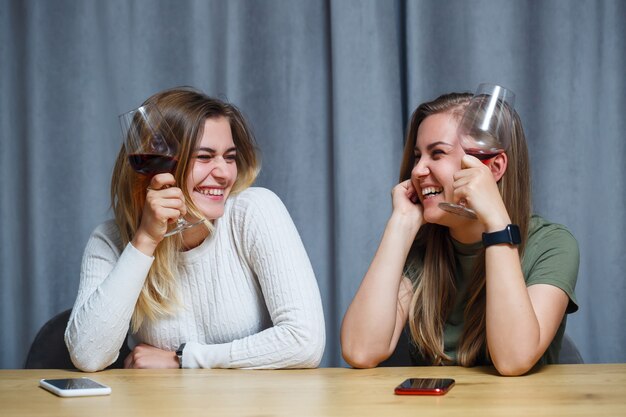 Due ragazze di aspetto europeo con i capelli biondi sono sedute al tavolo, bevono vino e ridono, si rilassano a casa, alcol